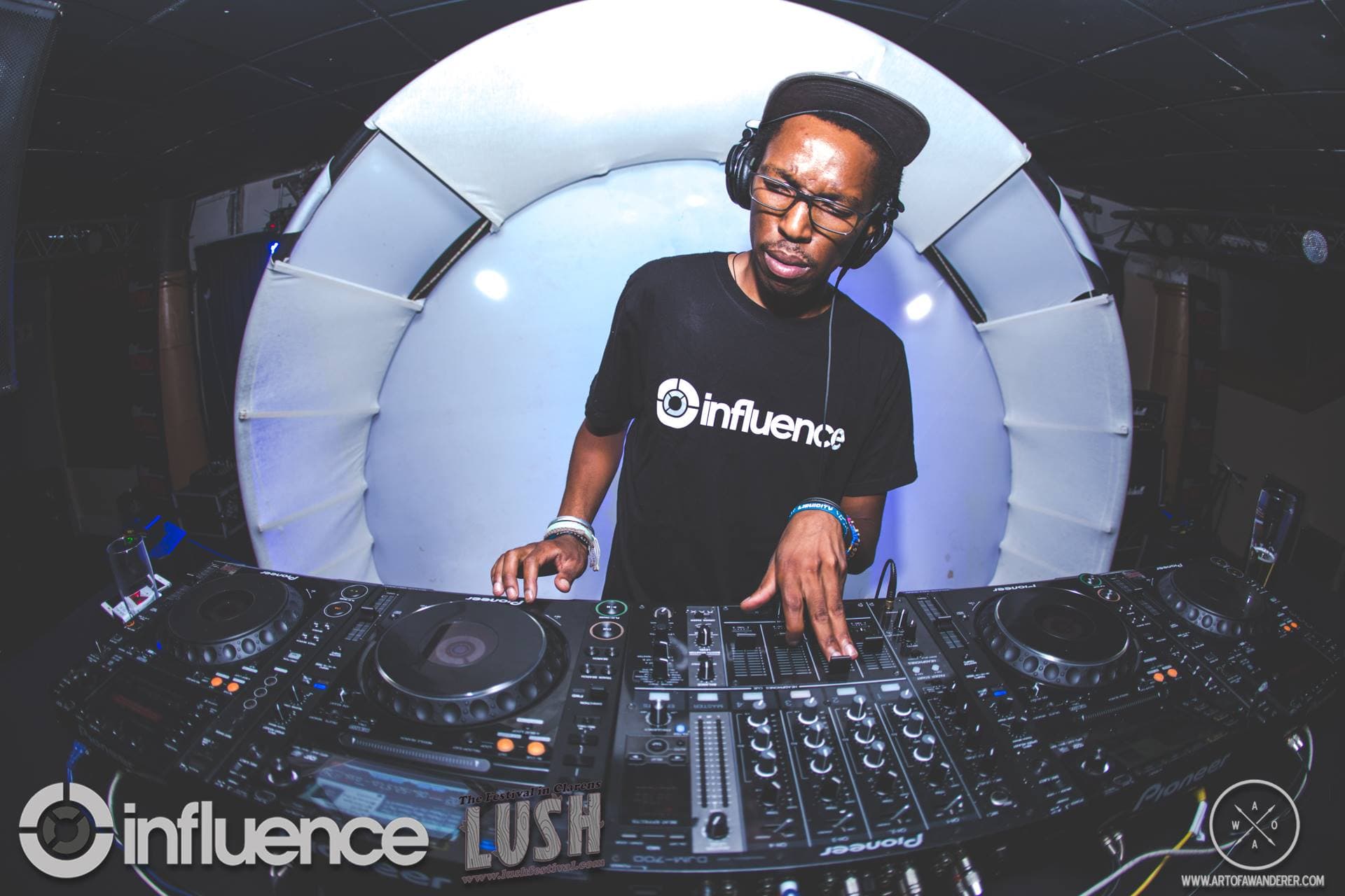 A fisheye shot of the DJ performing in front of a glowing white circular backdrop at a festival booth.
