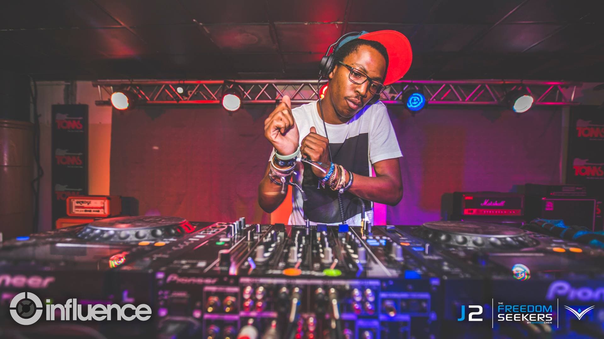 The DJ mid-gesture in a red cap under pink and blue stage lights.