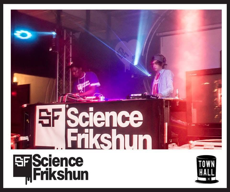 Two DJs play behind a booth branded "Science Frikshun" under blue laser beams and a red-pink glow.