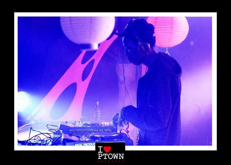 DJ in headphones seen in profile at the decks under purple and pink light, with paper lanterns behind.
