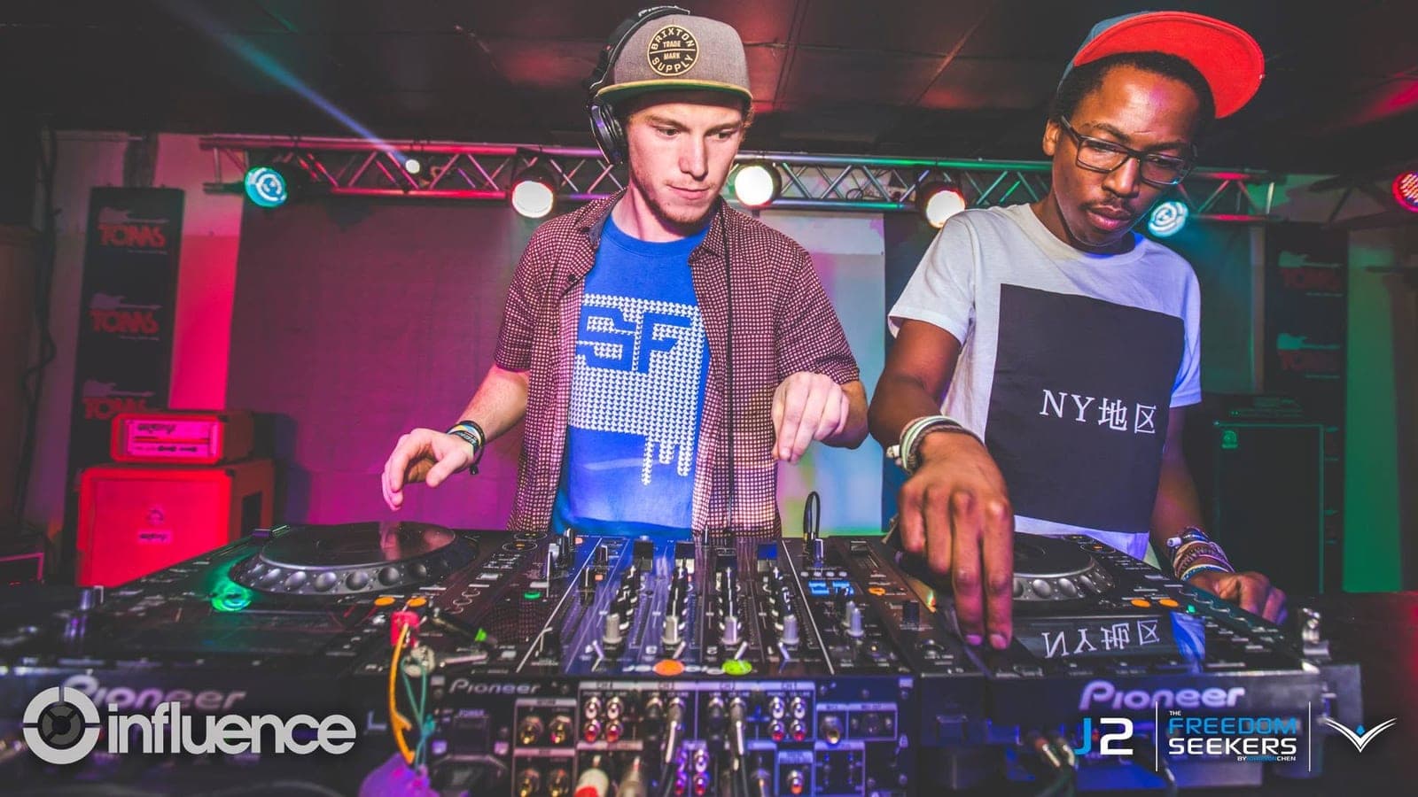 Two DJs at a Pioneer CDJ and mixer setup, one in an SF shirt and one in an "NY" tee with a red cap.