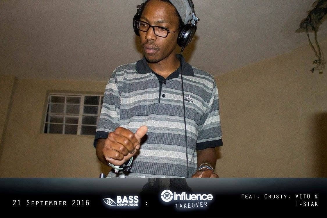 The DJ giving a thumbs up at the decks in a striped polo, glasses and headphones.