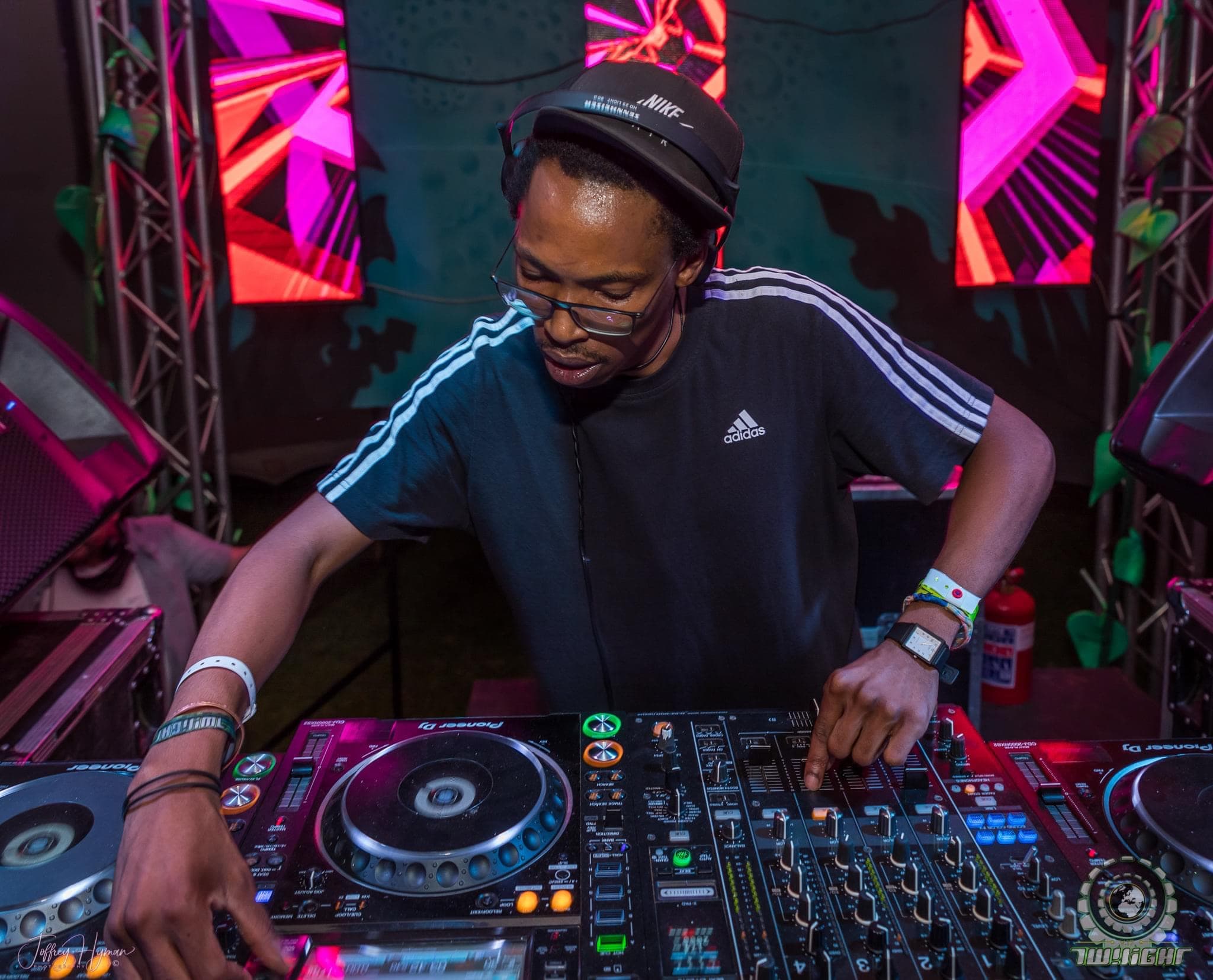 The DJ focused on the mixer on a festival stage lit with pink and red LED panels.