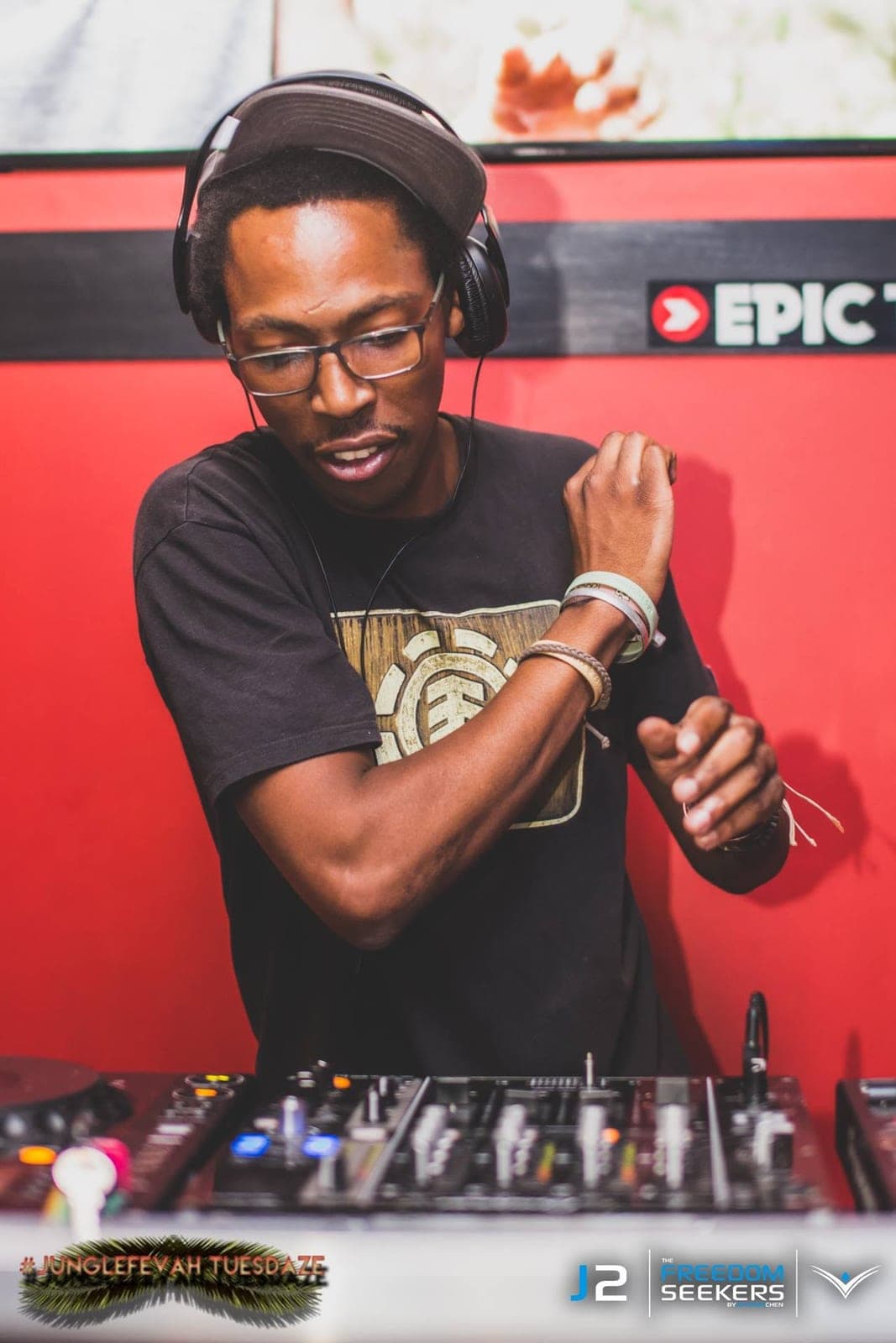 DJ in headphones, glasses and an Element t-shirt mid-gesture in front of a red wall.